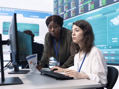 Diverse team of analysts examining monthly cost and revenue elements on a big screen, working on creating a financial projection for future improvements and success within the organization.